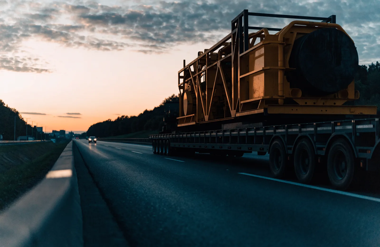 An oversize lowboy trailer hauling industrial machinery at dusk